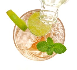 Closeup top view a glass of beverage with slice limes, mint and water flow from the glass bottle on white background, selective focus.