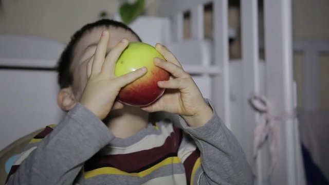The child eats an apple sitting at a table in the room