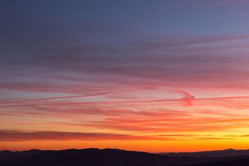 Clouds and jet vapor trails creating beautiful, colorful texture in the sky at sunset with mountain profiles on the low part of the frame