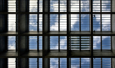 Looking up to the blue sky with clouds through roof windows with all light blinds opened but one closed.