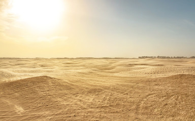 Fototapeta na wymiar Empty flat sahara desert, wind forming sand dust, with backlight sun in background. Douz, Tunisia
