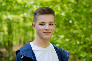 Smiling teenager in white T-shirt close-up. The young guy. Portrait of a young man on a natural background. Teenager. Student. Youth hairstyle.