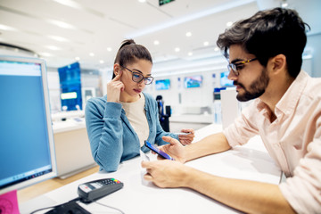 Beautiful young brunette talking with employe in the tech store.