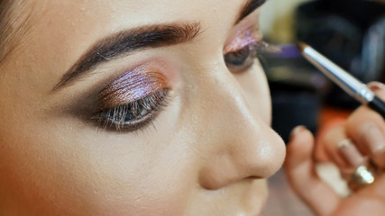 Girl makeup artist paints the eyes of the girl model. Stroke of upper eyelids.