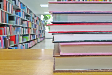 The old books on the wooden table in the library. Selective focus with blurred bookshelves and green leaves from the window background. Education and book's day concept. Selective focus.