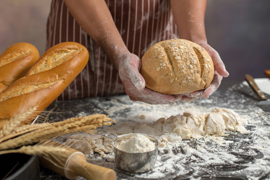 Chef holds the fresh bread in hand. Man preparing buns at table in kitchen
