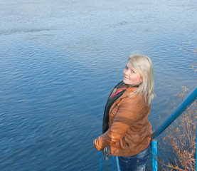 Fototapeta premium Blonde young girl by the river. Autumn Sunny day