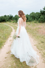 Fototapeta na wymiar bride in white llight wedding dress with bridal bouquet walking in lane, back view