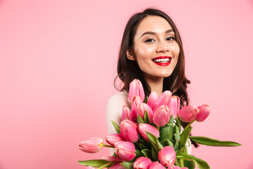 Obraz na płótnie Canvas Wonderful woman 20s with beautiful lovely look posing on camera holding bunch of spring tulips, isolated over pink background