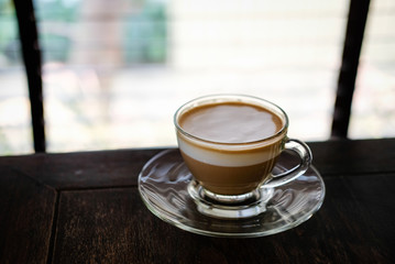 hot espresso macchiato coffee with milk topping in glass cup on wood table