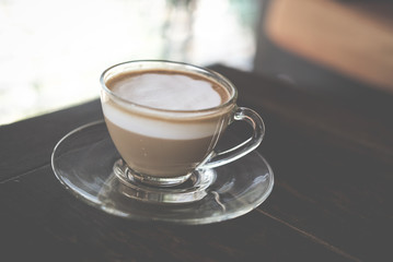 hot espresso macchiato coffee with milk topping in glass cup on wood table