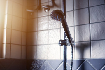 Naklejka na ściany i meble Shower head with running water in a bathroom with morning sun light. Take a bath in morning time. 