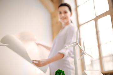 Alternative energy. Selective focus of wind mill models with brunette pregnant woman staying and studying blueprint