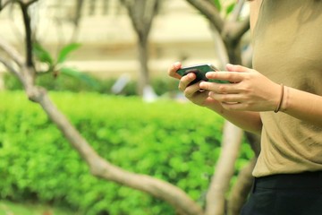 Asian woman holding and use wifi internet on mobile phone at the park. Park and technology concept.