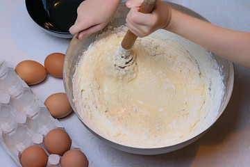 Children's hands knead the dough for pancakes, eggs and black cups