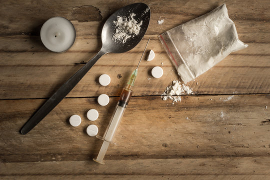Drugs, powder, spoon, and tablets on rustic wooden background. Drug addiction concept background with space for text
