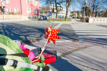 Rear view of a baby stroller with red pinwheel at pedestrian crossing.