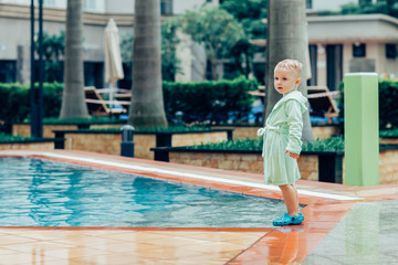 Serious little boy standing at swimming pool