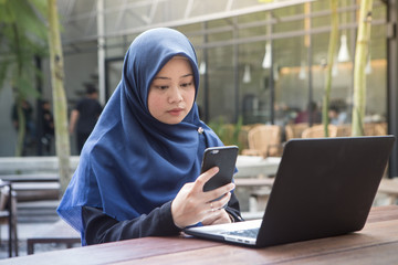 Southeast asian hijab woman using her smartphone and laptop computer at outdoors cafe - 195450487