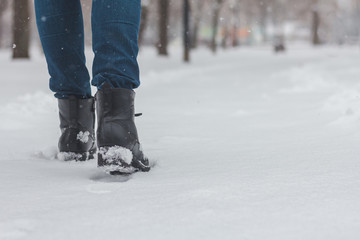 Legs of woman walking in winter park evening. Girl boots walking snow weather. Closeup of winter shoes. Background with snow and copy space area for a text.