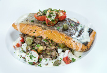 Grilled salmon, sesame seeds and marjoram on a white plate. Marinated tomatoes. Garnish. View from the bokku. Studio shot