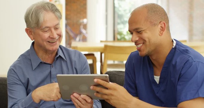 4K Happy elderly man with friendly healthcare worker, teaching him how to use computer at home. Slow motion