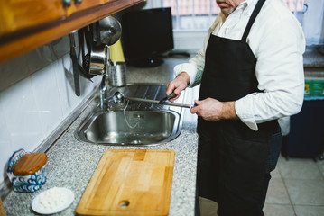 Man of 59 year old sharpen knife in the kitchen of his house.