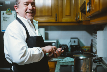 Fototapeta na wymiar Man of 59 year old with smartphone in the kitchen of his house.