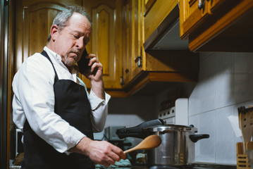 Man of 59 year old with smartphone in the kitchen of his house.