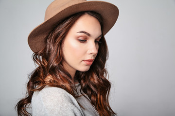 Horizontal portrait of stylish attractive female model wears summer clothes and brown hat with natural makeup posing on gray background in studio. Looking at camera