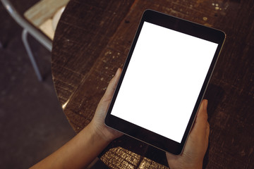 Topview image of hands holding black tablet pc with blank white desktop screen on vintage wooden table