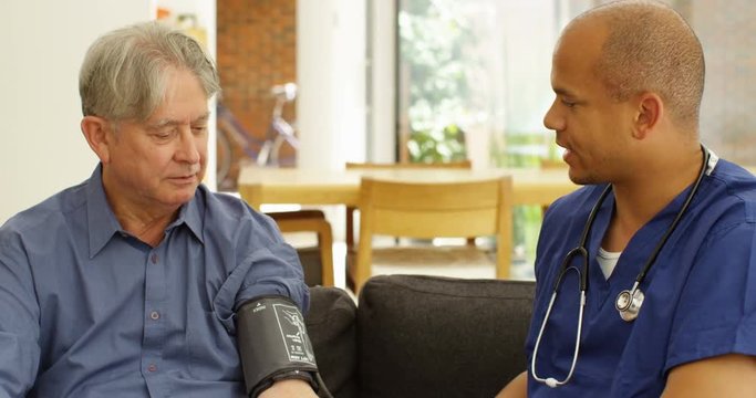 4K Friendly male community nurse checking blood pressure of elderly man at home. Slow motion