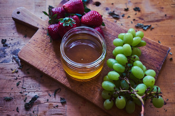 Honey in jar with strawberries and green grapes on wooden plate