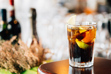 Closeup View of Glass of Cuba Libre Cocktail decorated with Lime and Lemon at lighted Bar Counter Background