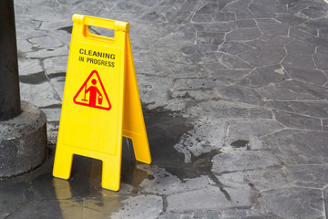 wet floor sign, yellow plastic sidn on wet stone floor with cleaning in progress text