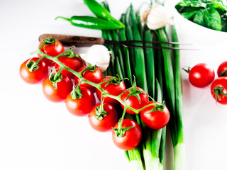 Little branch of cherry tomatoes, bowl of spinach, green hot peppers,onion leaves, garlic and fork over white isolated background.