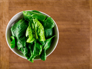 White ceramic bowl with fresh spinach over wooden table background.