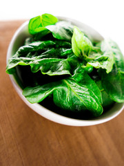 White ceramic bowl with fresh spinach over wooden table background.