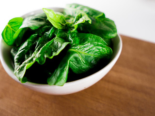 White ceramic bowl with fresh spinach over wooden table background.