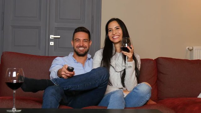 A young couple watching TV together on the sofa and having fun.
