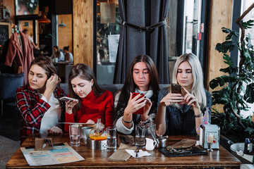 Four stylish young woman with coffee seated at a table in cafe