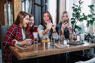 four young women sitting in cafe using smart phone and having funny conversation.