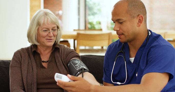 4K Friendly smiling doctor checking patient's blood pressure on home care visit. Slow motion