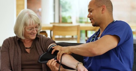 4K Friendly community nurse checking patient's blood pressure on home care visit. Slow motion - Powered by Adobe