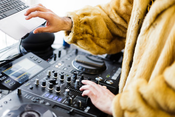 Dj hands on equipment deck and mixer with turntable at party. Dj dressed in a fur coat. closeup