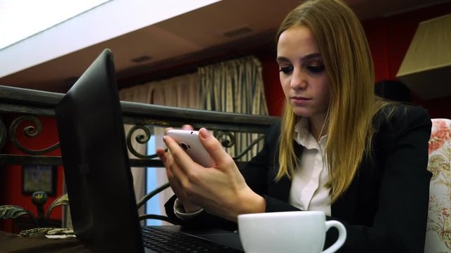 Business Girl in a cafe with a laptop and smartphone overwritten in the messenger