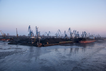 Fototapeta premium Freight shipping containers and gas oil tanks at the docks. in import export and business logistic. Cargo ship docked at at the port. Cargo cranes by winter evening in the Port Riga, Latvia.