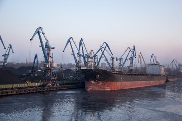 Freight shipping containers and gas oil tanks at the docks. in import export and business logistic. Cargo ship docked at at the port. Cargo cranes by winter evening in the Port Riga, Latvia.