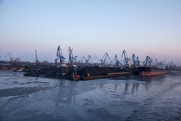 Fototapeta premium Freight shipping containers and gas oil tanks at the docks. in import export and business logistic. Cargo ship docked at at the port. Cargo cranes by winter evening in the Port Riga, Latvia.