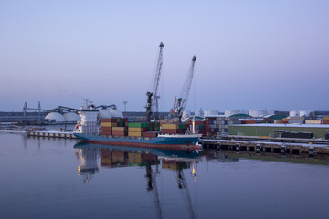 Freight shipping containers and gas oil tanks at the docks. in import export and business logistic. Cargo ship docked at at the port. Cargo cranes by winter evening in the Port Riga, Latvia.